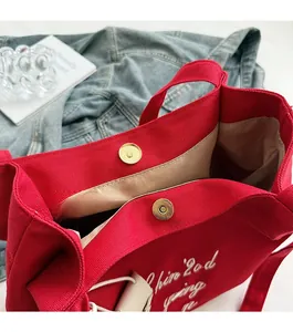 Gros plan du sac cabas en toile rouge montrant le fermoir magnétique et la broderie
