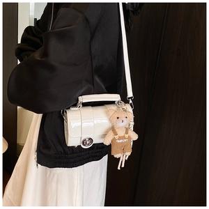 Detail of white cylinder shoulder bag with glossy patent leather and a cute bear charm