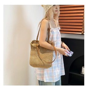 Detail of hand-woven straw tote bag showing brown leather strap and scalloped edge finish