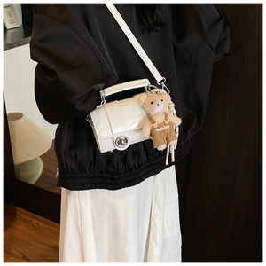 Detail view of white patent leather crossbody bag with silver lock and plush bear charm