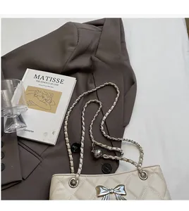 Detail of quilted beige bag with silver bow clasp and woven metal chain strap