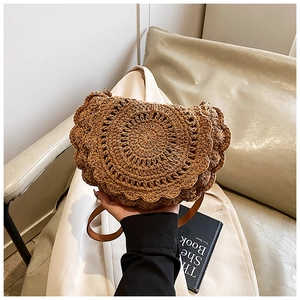 Close-up of woven straw saddle bag with wavy scalloped edges and brown leather strap