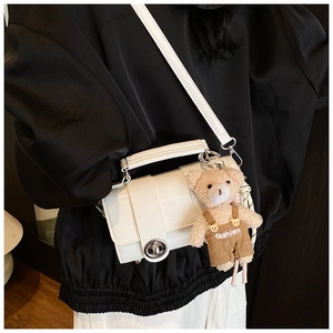Close-up of white glossy crossbody bag with silver lock and plush bear ornament