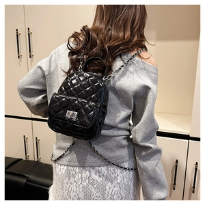 Detail of black quilted patent leather backpack with silver lock and chain straps