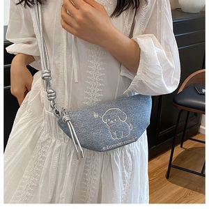 Détail d'un sac demi-lune en denim bleu clair avec broderie chiot et bandoulière corde