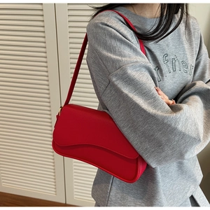 Detail view of a vibrant red pebbled leather shoulder bag shown on a model