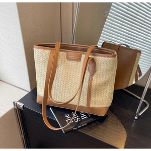 Detail of woven straw tote bag with brown leather handles and brand tag on a desk