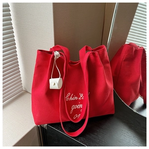 Détail du cabas en toile rouge avec broderie blanche et un mini charm en cuir sur la poignée