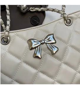 Close-up of beige quilted bag featuring silver bow detail and metal ball chain strap