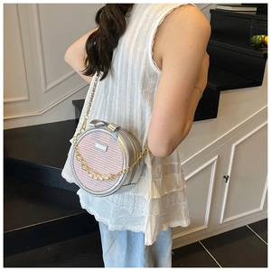 Detail view of pink tweed round crossbody bag with bow and pearl chain on a model