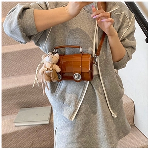 Brown patent leather cylindrical crossbody bag with metal buckles and cute teddy bear charm