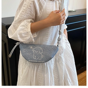 Détail du sac croissant en denim bleu avec broderie chiot et bandoulière à nœud tissé
