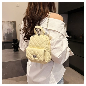 Close-up of cream yellow quilted mini backpack with silver chain strap on a model