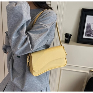 Detailed shot of yellow pebbled leather shoulder bag with asymmetrical flap on model