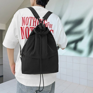Rückansicht eines schwarzen Nylon-Kordelzug-Rucksacks am Modell vor weißer Ziegelwand