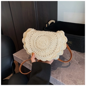 Close-up of the handcrafted crochet texture and brown leather strap on a beige saddle bag
