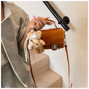 Detailed shot of brown glossy cylinder bag with metal lock and cute teddy bear charm