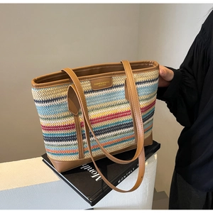 Detail of multi-color woven straw tote bag featuring a leather logo patch and brown handles