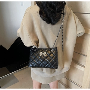 Detail of black quilted chain bag featuring a silver bow accessory and woven strap