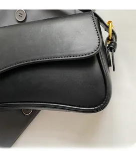 Détail du rabat d'un sac besace noir avec surpiqûres précises et boucle dorée en métal