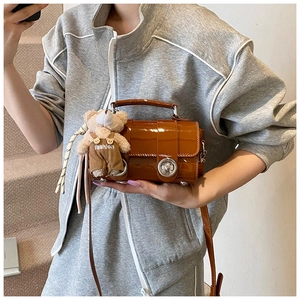 Detail of caramel glossy patent leather handbag featuring a plush bear charm and metal clasp