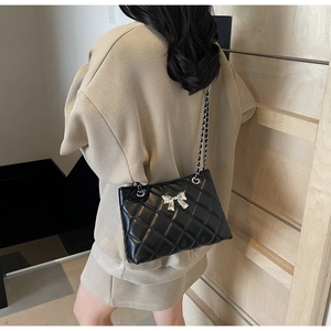 Detail of black quilted leather shoulder bag with silver bow buckle and chain strap