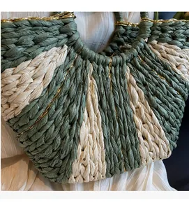 Close-up of woven straw tote bag featuring green and white geometric patterns with gold thread