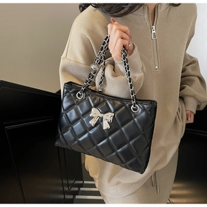 Detail of black quilted shoulder bag featuring silver metal bow and leather chain strap