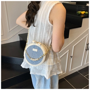 Detail of round crossbody bag with blue houndstooth pattern and pearl accents worn by model