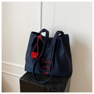 Détail du sac cabas en toile marine avec broderie rouge et petit charme de porte-monnaie
