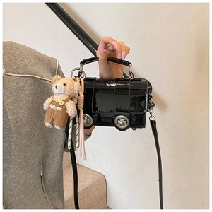 Detail of black patent leather crossbody pillow bag featuring silver rings and bear charm
