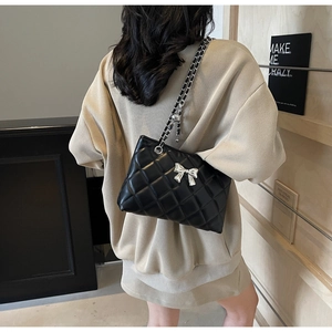 Detail of black quilted leather shoulder bag with silver bow and chain strap on model