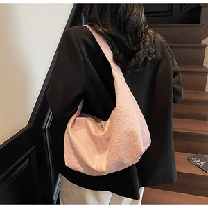 Pink lychee grain leather hobo bag worn with black suit on stairs in close-up detail