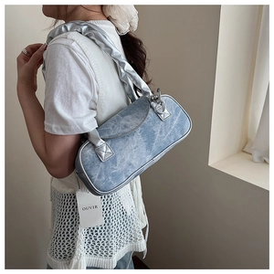 Dettaglio borsa a spalla in denim blu con manico a pieghe argento ed etichetta OUVIR