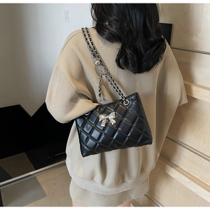 Rear view of model wearing a black quilted crossbody bag with silver bow accent