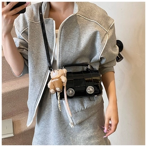 Detail of black patent leather crossbody bag with silver buckles and plush bear charm