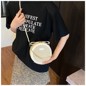 Detail of round straw crossbody bag featuring cream bow and pearl chain strap accents