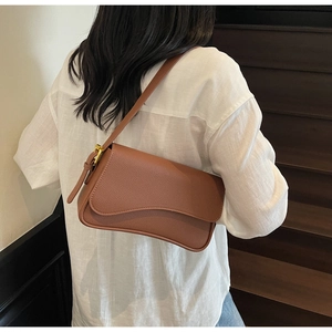 Detail of dark brown litchi pattern leather underarm bag with gold buckle on a model