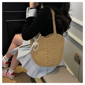 Detail of woven khaki tote bag with pearl lace charm shown on a model for daily style