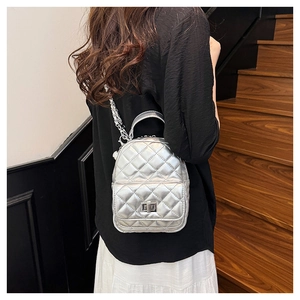 Detail view of a silver quilted mini backpack with chain straps on a model's back
