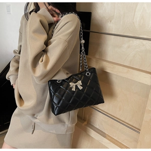 Detail view of black quilted crossbody bag with silver bow accent and chain strap