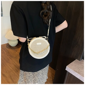 Detail of round straw crossbody bag with white leather trim and pearl chain on a model