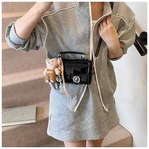 Detail of glossy black patent leather pillow bag with cute plush bear charm on strap