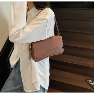 Detailed side view of a brown leather baguette bag with a stylish wavy flap design