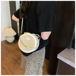 On-body view of a white round woven bag featuring pearl gold chain and leather strap