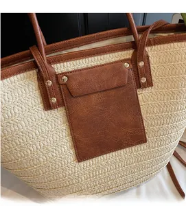 Detailed close-up of straw tote bag with brown faux leather trim and metallic rivets
