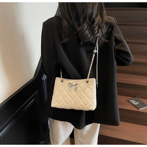Detail of beige quilted shoulder bag with silver bow and leather chain strap on a model