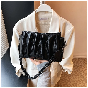 Detail of black pleated cloud bag with glossy finish and woven handle ornament