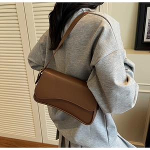 Détail d'un sac à bandoulière marron foncé avec rabat ondulé et sangle ajustable