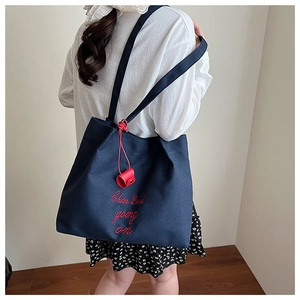 Détail du grand sac cabas en toile bleu marine avec broderie rouge porté à l'épaule